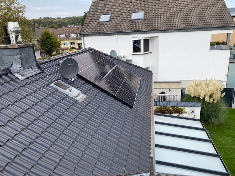 Blick über ein dunkles Ziegeldach in Aldenhoven mit Solarmodulen neben der Satellitenschüssel, dahinter Nachbarhaus und Garten