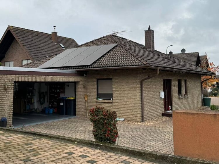 Bungalow aus hellem Klinker in Niederzier mit Solarmodulen auf zwei Dachflächen, davor offene Garage und gepflasterte Einfahrt